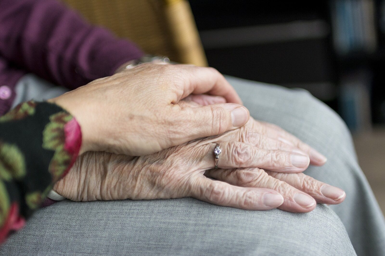 Hand liegt tröstend auf den Händen einer älteren Person