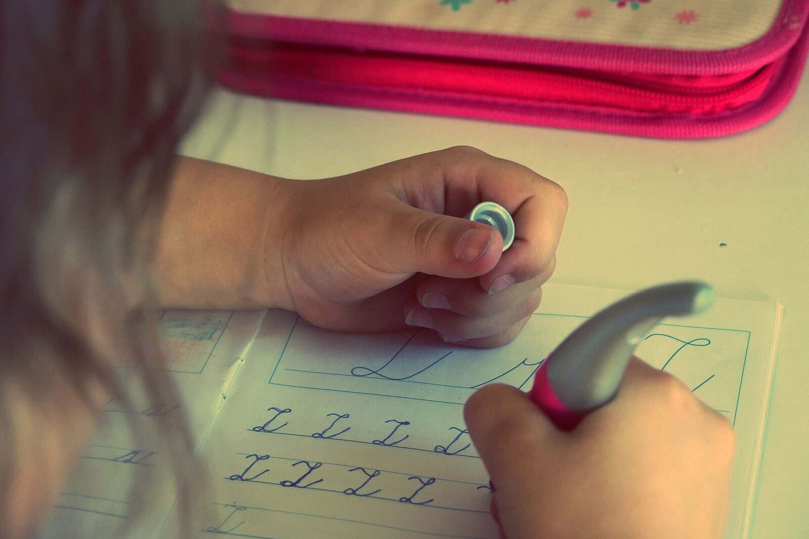 Kind schreibt mit Bleistift Buchstaben in Schreiblinien