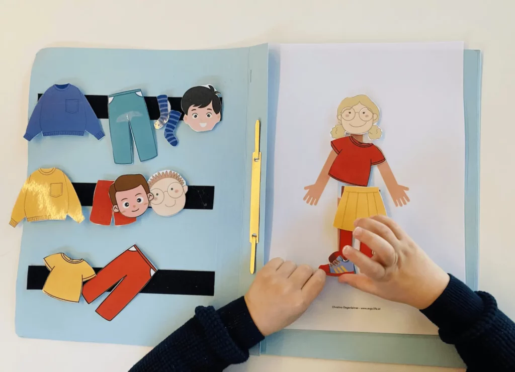 Kind ordnet in der TEACCH-Aufgabenmappe Kleidungsstücke einer Figur zu