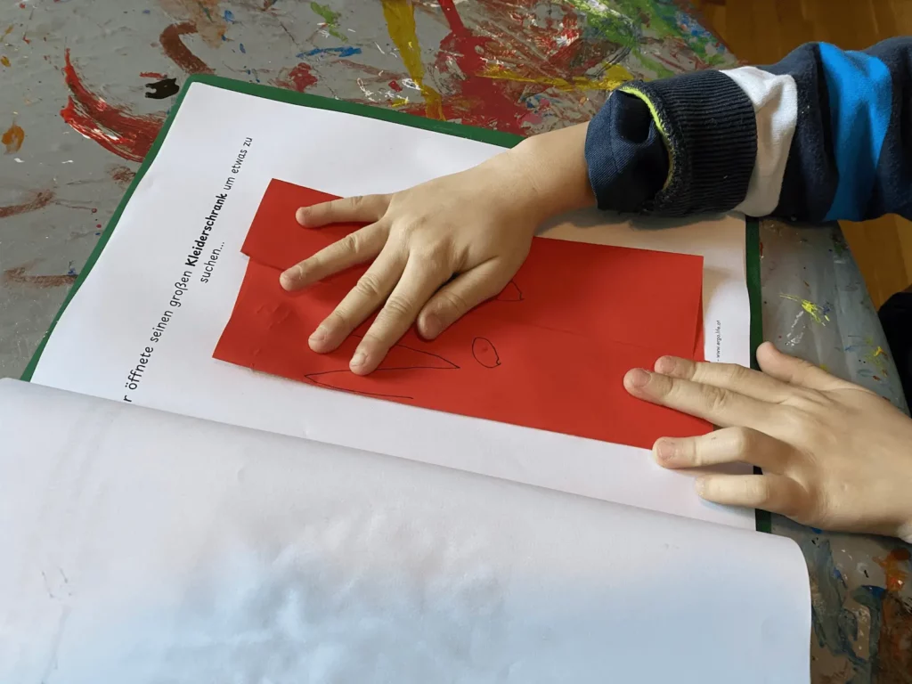Kinderhände falten rotes Papier auf der Vorlage der Faltgeschichte
