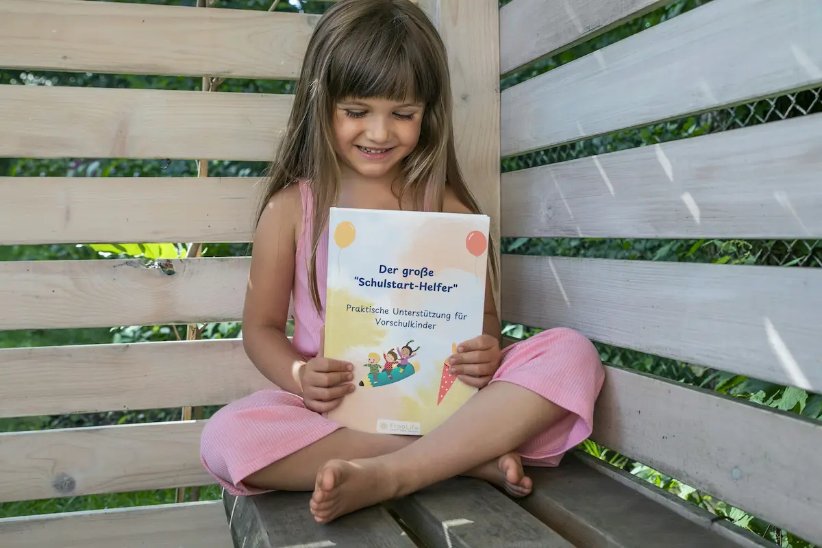 Mädchen sitzt auf einer Bank und liest im großen Schulstarthelfer