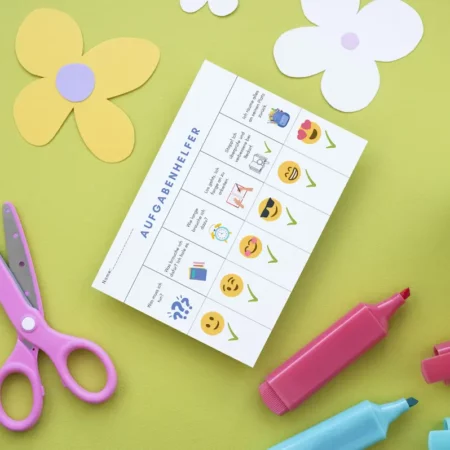Aufgabenhelfer-Karte mit Smileys neben rosa Schere und Filzstiften auf grünem Papier