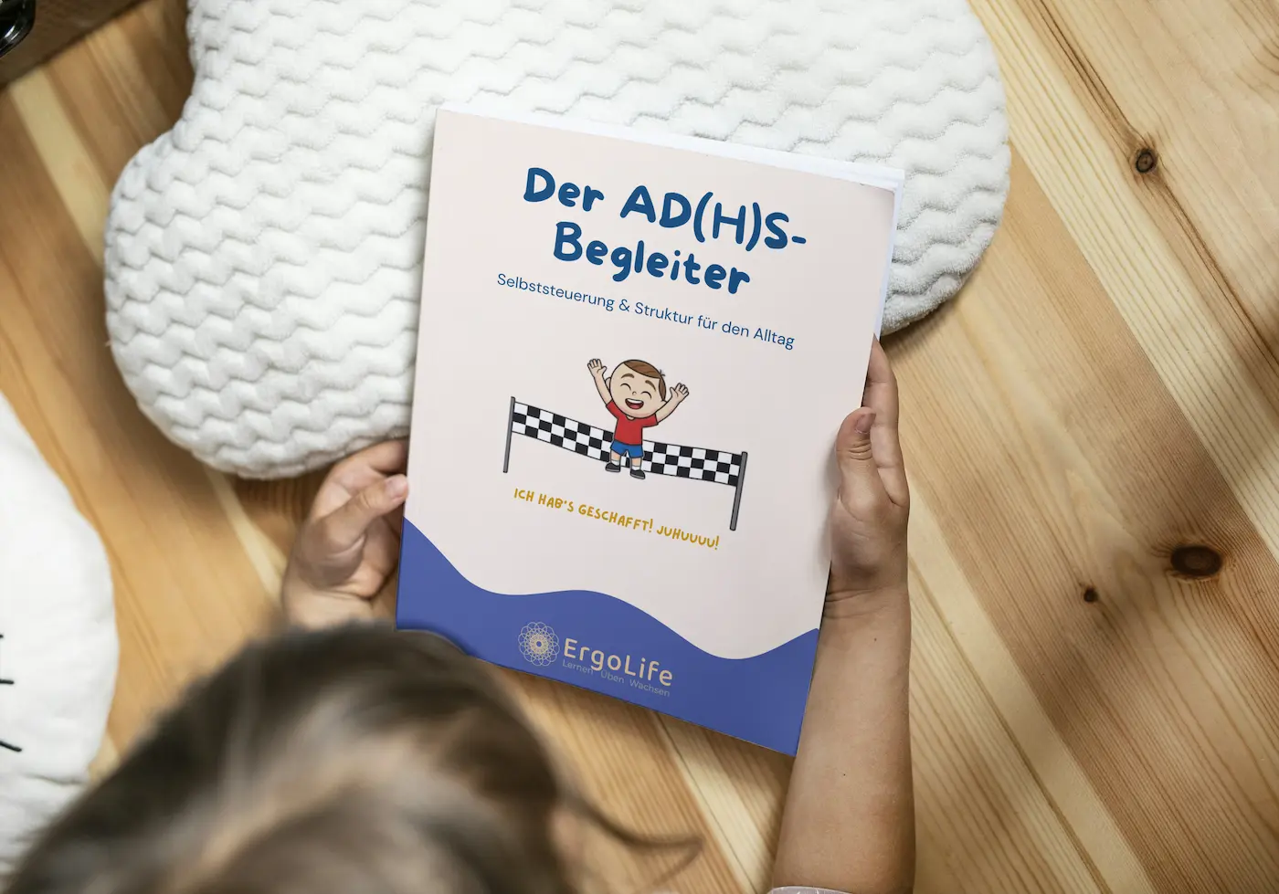 Kind hält das Heft „Der AD(H)S-Begleiter“ über einem Holzboden